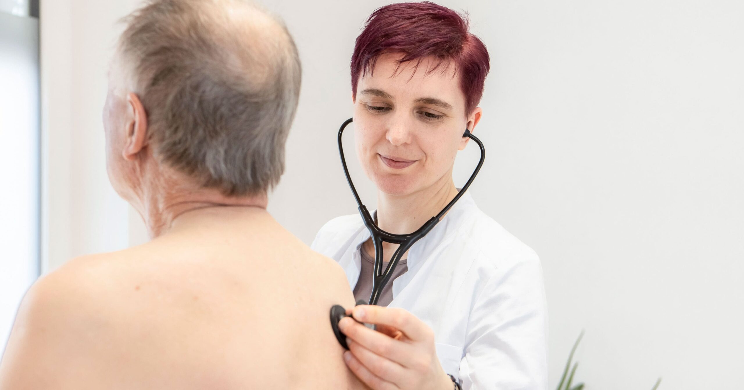 Dr. Dissauer hört mit dem Stethoskop einen älteren Mann am Rücken ab