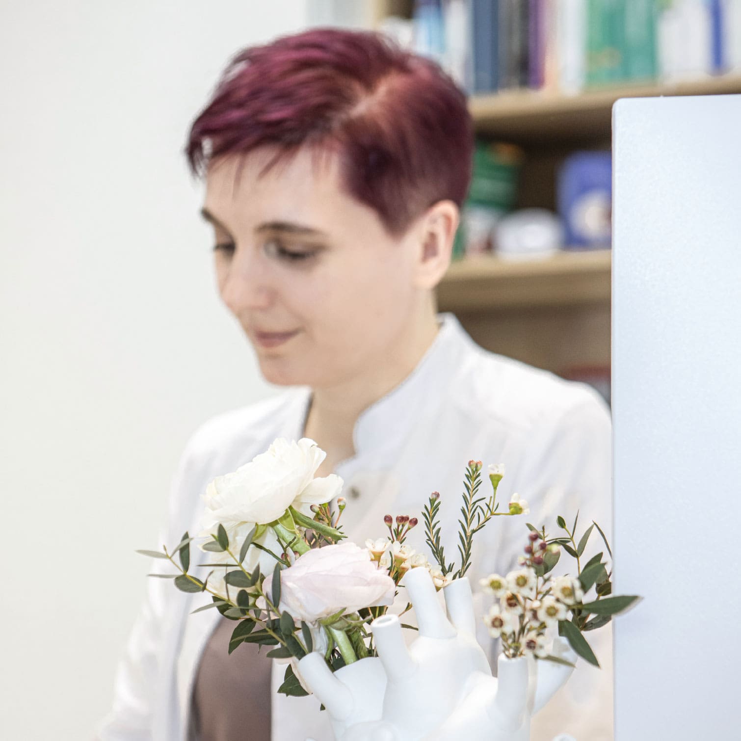 Dr. Dissauer, eine Dame im Arztkittel mit rötlich gefärbten Haaren, im Vordergrund eine Blumenvase