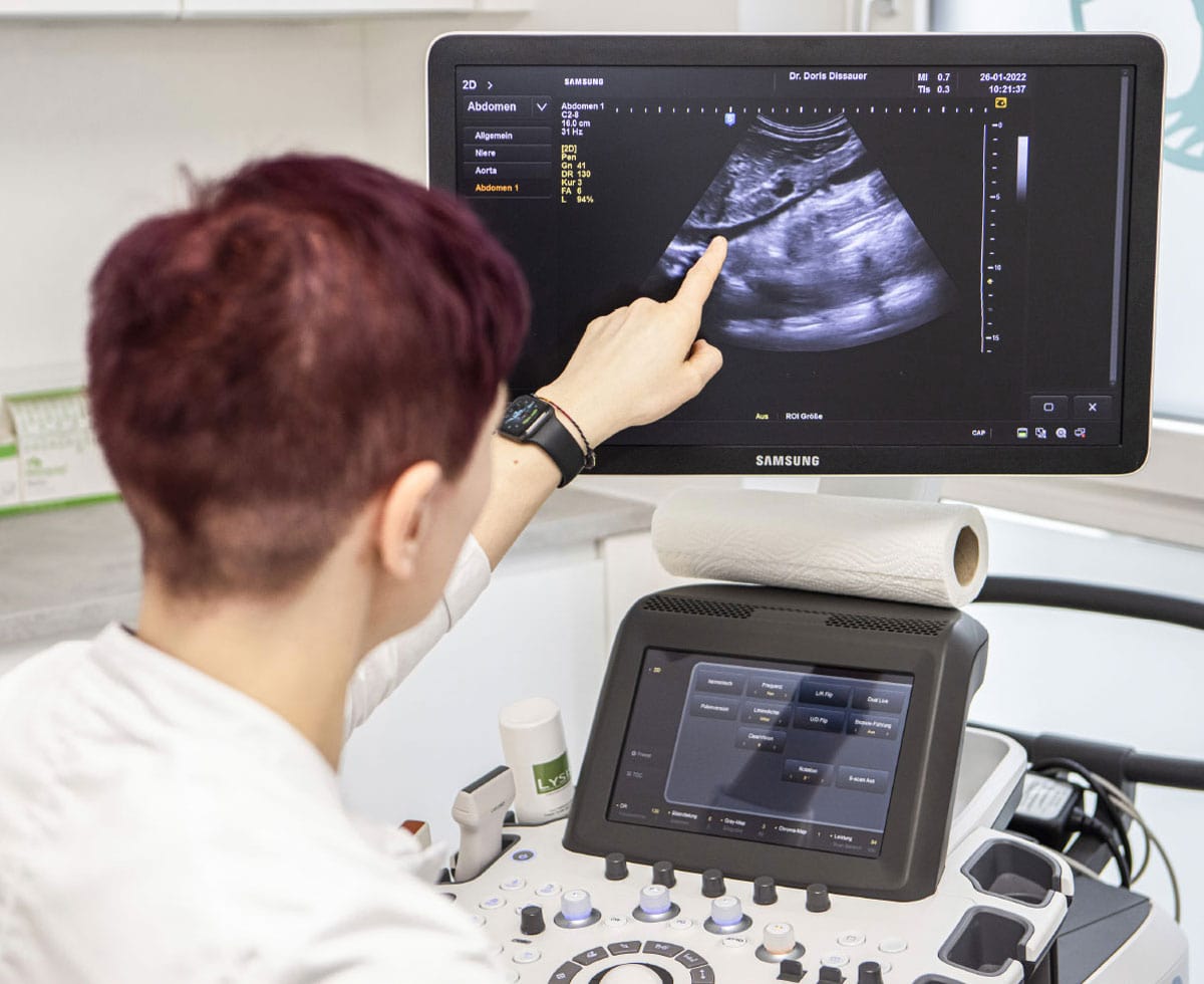 Dr. Dissauer zeigt auf einen Bildschirm, auf dem ein Ultraschallbild erkennbar ist